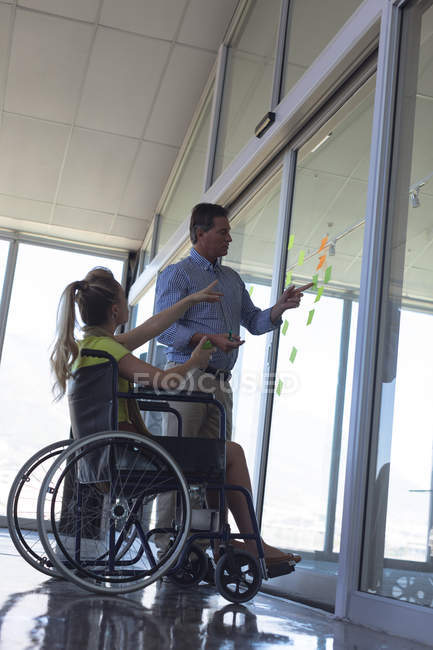 Side view of disabled Caucasian blonde female and male executive discussing over sticky notes in the office — Stock Photo