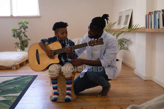 Frontansicht eines afrikanisch-amerikanischen Vaters, der seinem Sohn hilft, zuhause Gitarre zu spielen — Stockfoto