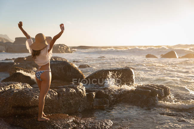Rückansicht einer Frau, die an einem sonnigen Tag mit offenem Arm am Strand steht — Stockfoto