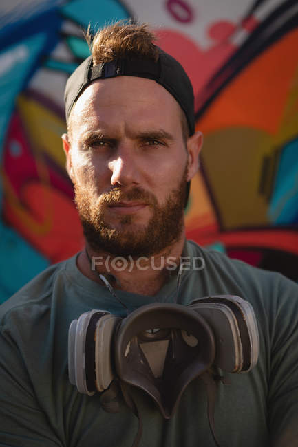 Portrait of young Caucasian graffiti artist standing with protective mask. He is looking at camera — Stock Photo