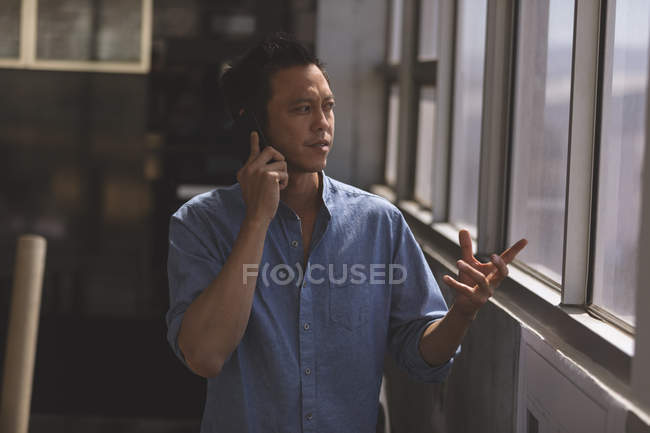 Vorderseite eines asiatischen männlichen Architekten, der in einem modernen Büro mit dem Handy spricht — Stockfoto