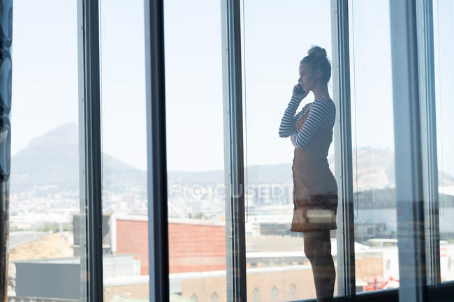 Вид сбоку молодая кавказская блондинка-бизнесвумен разговаривает по мобильному телефону в офисе — стоковое фото