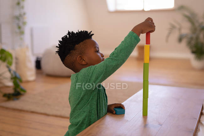 Vista lateral de pequeño niño afroamericano lindo jugando con el juguete en casa - foto de stock