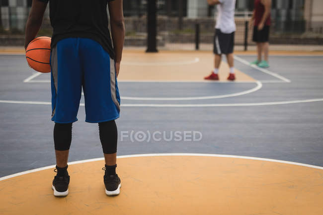 Низька частина баскетболіста, який тримає баскетбол на ігровому майданчику проти гравців у фоновому режимі — стокове фото