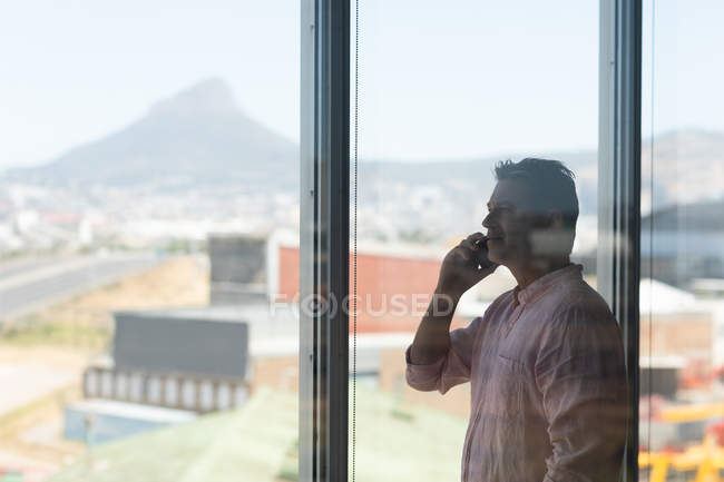Вид сбоку зрелого кавказского бизнесмена разговаривающего по мобильному телефону в офисе — стоковое фото