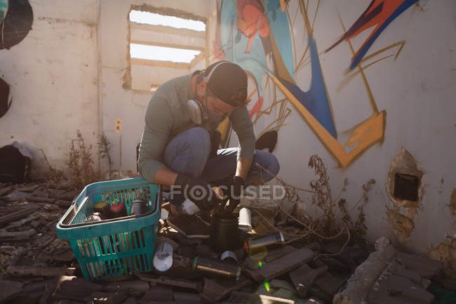 Front view of young Caucasian graffiti artist filling graffiti color in aerosol spray while crouching — Stock Photo