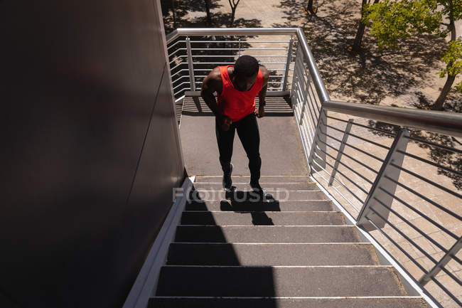 Hochwinkelaufnahme eines jungen afrikanisch-amerikanischen fitten Mannes, der an einem sonnigen Tag von einer Brücke rennt — Stockfoto