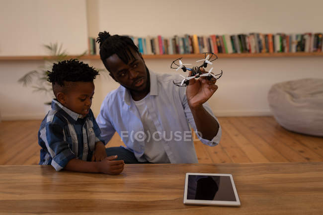 Vista frontal do pai e do filho afro-americanos brincando com drone na mesa em casa — Fotografia de Stock