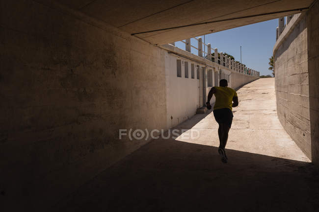 Вид сзади на молодого афроамериканца, бегущего под мостом в солнечный день — стоковое фото