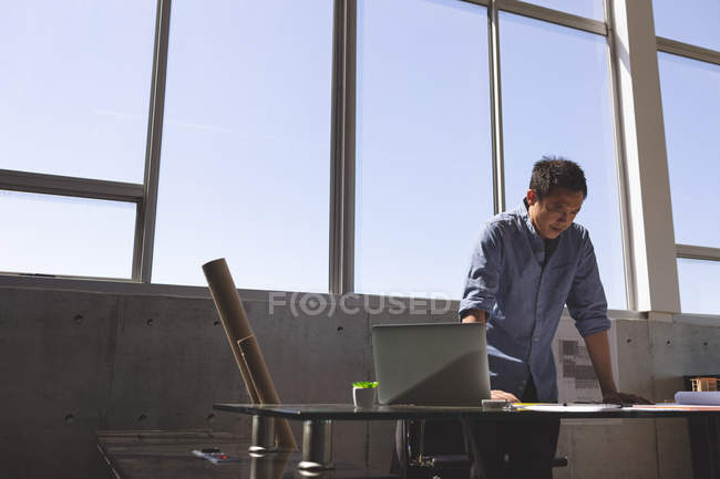 Vista frontal do arquiteto masculino asiático em pé na mesa e olhando o modelo em um escritório moderno — Fotografia de Stock