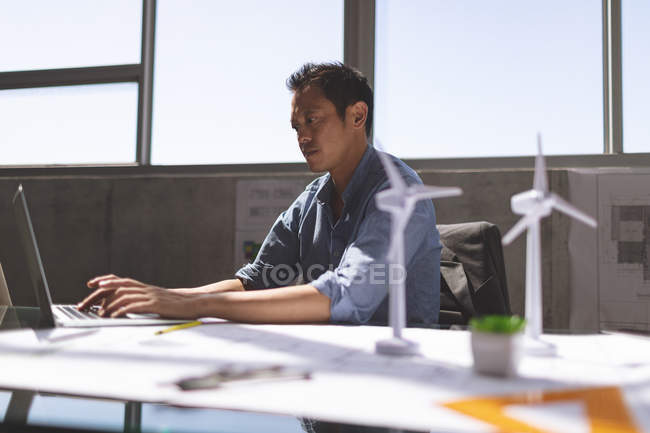Vista laterale dell'architetto asiatico di sesso maschile che lavora su laptop alla scrivania in un ufficio moderno — Foto stock