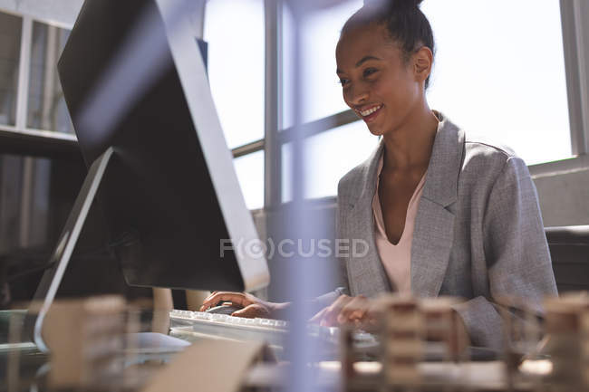 Низкий угол зрения улыбается смешанной расы деловая женщина, работающая за компьютером на столе в офисе — стоковое фото