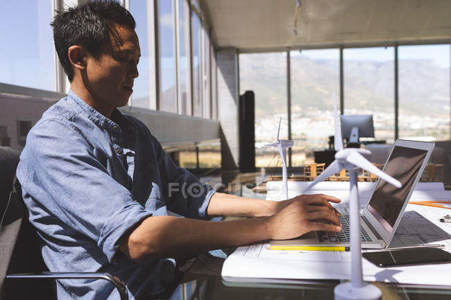 Вид сбоку молодого азиатского мужчины-руководителя, использующего ноутбук в архитектурном офисе — стоковое фото