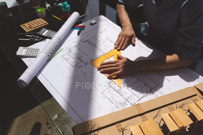 Высокий угол обзора молодого архитектора-мужчины, работающего над проектом с линейкой треугольника за столом в современном офисе — стоковое фото