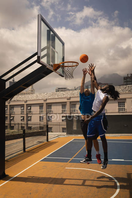Front view of multi-ethnic basketball players playing basketball at basketball court while they are jumping to score a hoop — Stock Photo