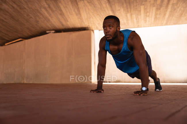 Vista de bajo ángulo del joven afroamericano en forma haciendo ejercicio de push-up bajo el puente - foto de stock