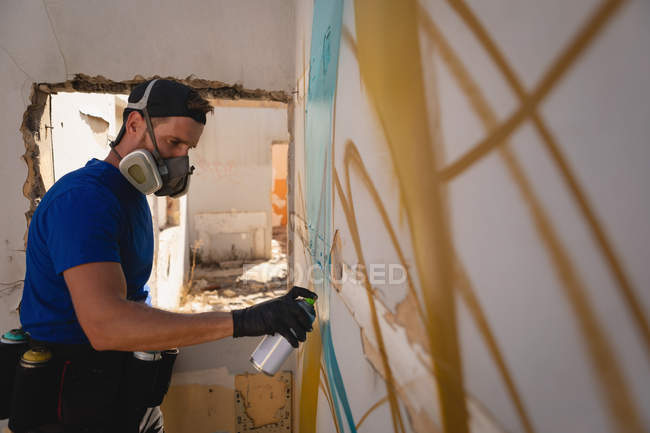 Vista lateral do jovem artista de graffiti caucasiano pintura spray sala de parede resistido — Fotografia de Stock