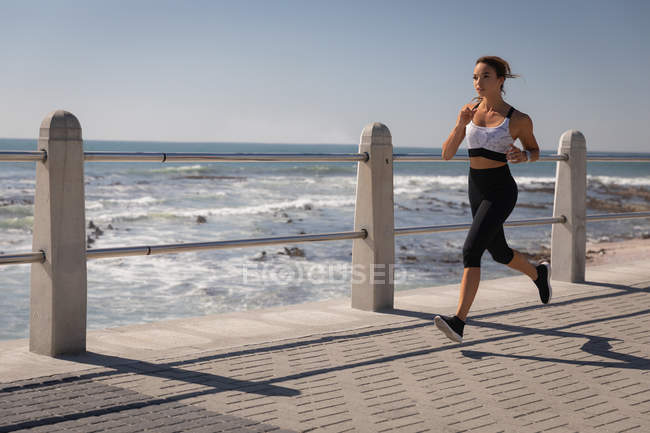 Seitenansicht einer Frau, die an einem sonnigen Tag auf der Strandpromenade läuft — Stockfoto