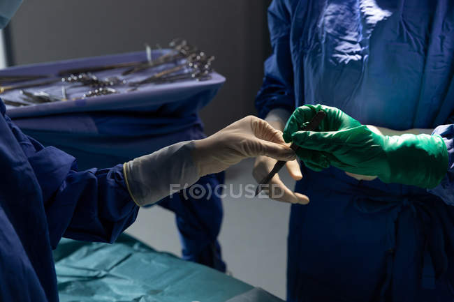 Primer plano de los cirujanos con cuchillo quirúrgico en quirófano durante la cirugía en el hospital - foto de stock