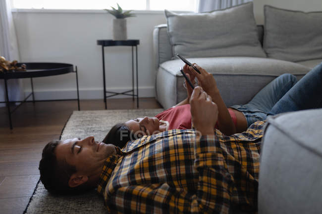 Side view of young multi-ethnic couple using mobile phone while relaxing on floor at home — Stock Photo