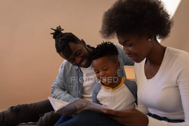 Вид сбоку на счастливую афроамериканскую семью, сидящую вместе и читающую сказку дома — стоковое фото