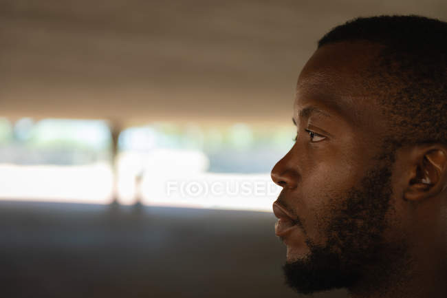 Vue latérale d'un jeune homme en forme afro-américain réfléchi debout sous le pont — Photo de stock