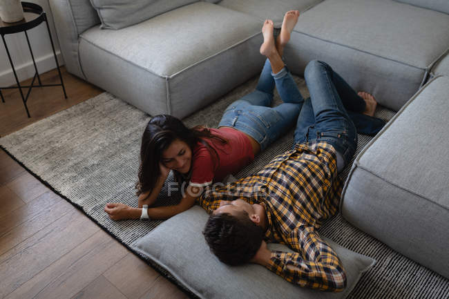 Blick aus der Vogelperspektive auf junge multiethnische Paare, die miteinander interagieren, während sie zu Hause auf dem Boden liegen — Stockfoto