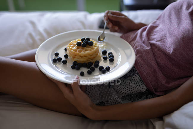 Parte centrale della donna che fa colazione sdraiata sul letto a casa — Foto stock