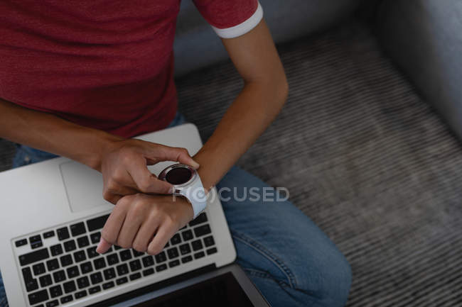 Vista de ángulo alto de la mujer que comprueba el tiempo mientras usa el ordenador portátil sentado en el suelo en casa - foto de stock