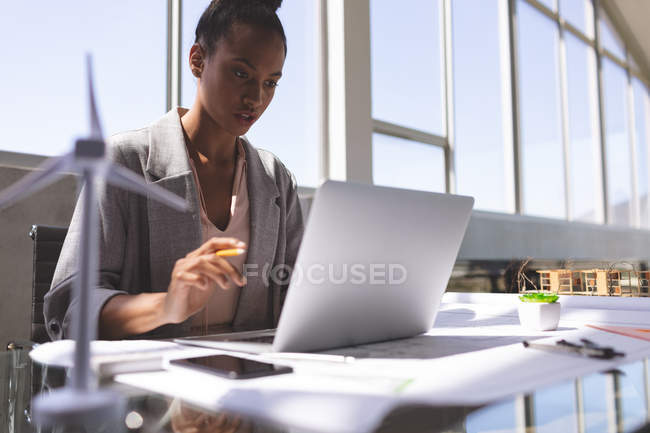 Front view of mixed race businesswoman using laptop at desk in architectural office — Stock Photo