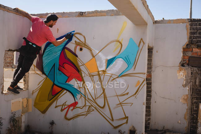 Vista trasera de la joven artista de graffiti caucásico pintura en aerosol en la sala de pared erosionada - foto de stock