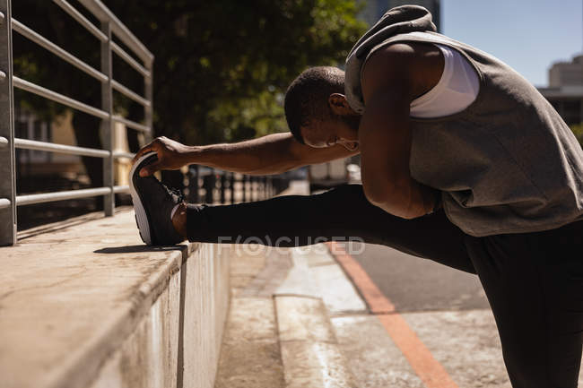 Vista lateral do jovem afro-americano em forma de homem fazendo exercício na rua — Fotografia de Stock