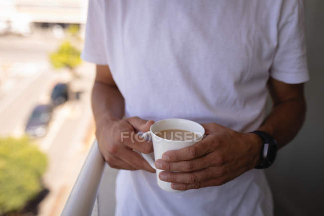 Средняя секция человека с чашкой кофе, стоящей на балконе дома — стоковое фото