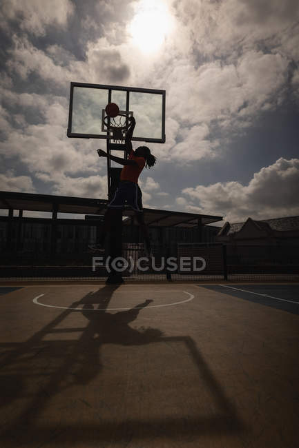 Side view of African-American basketball player playing basketball at basketball court in back lit — Stock Photo
