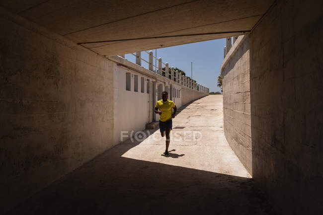 Front view of young African-American fit man running under the bridge on a sunny day — Stock Photo