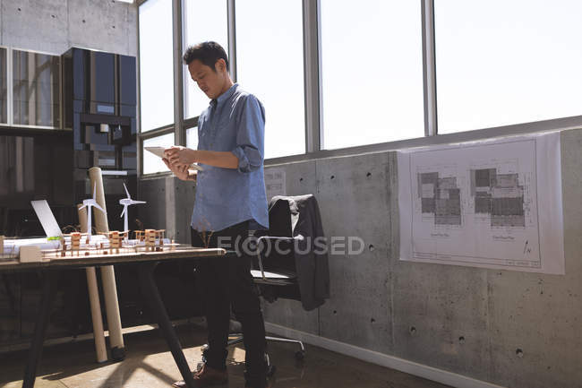 Vista frontal de un joven ejecutivo asiático usando tableta digital en la oficina de arquitectura - foto de stock