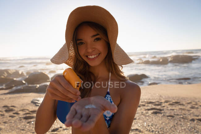 Portrait of woman holding body lotion in her hand at beach. She is looking and smiling at camera — Stock Photo