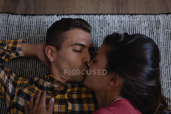 Vista de ángulo alto de la pareja multiétnica besándose mientras yacen en el sofá en casa - foto de stock