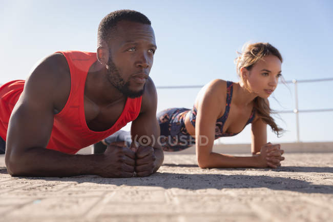 Vista lateral de una joven pareja multiétnica haciendo ejercicios de planchado en el pavimento - foto de stock