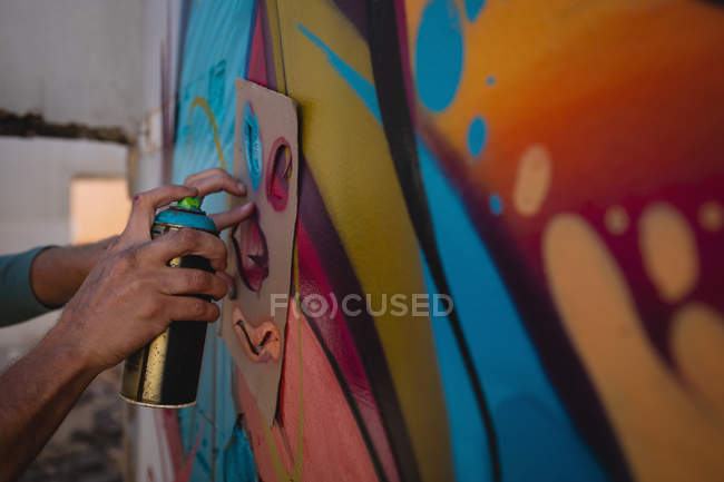 Side view of young Caucasian graffiti artist spray painting on card board at alley — Stock Photo