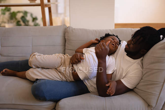 Front view of African-American father and son enjoying while lying on sofa at home — Stock Photo