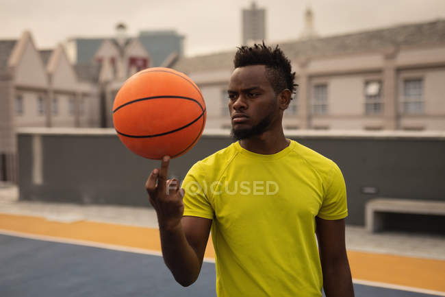 Vista frontal del jugador de baloncesto afroamericano balanceando la pelota en el dedo en la cancha de baloncesto - foto de stock