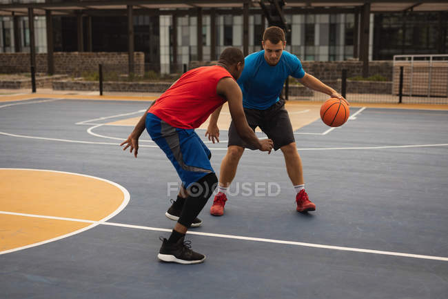 Front view of multi-ethnic players playing basketball at basketball court — Stock Photo