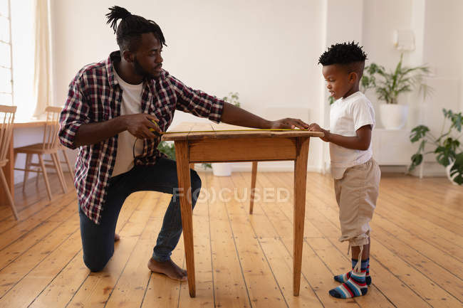 Vista lateral da mesa de medição de pai e filho afro-americano com fita métrica — Fotografia de Stock