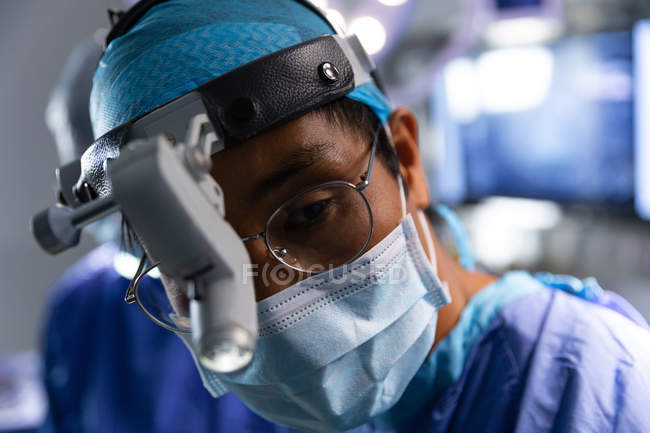Primer plano del cirujano asiático concentrado en quirófano durante la cirugía en el hospital - foto de stock