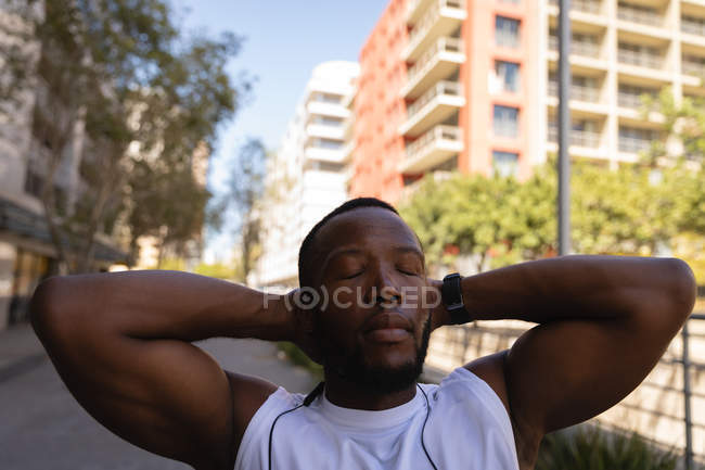 Vorderansicht eines jungen afrikanisch-amerikanischen fitten Mannes, der es sich auf der Straße mit der Hand hinter dem Kopf gemütlich macht — Stockfoto