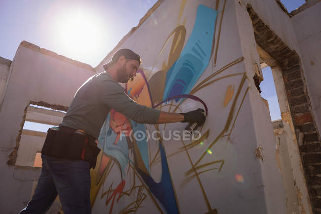 Low angle view of young Caucasian graffiti artist spray painting on weathered wall room — Stock Photo