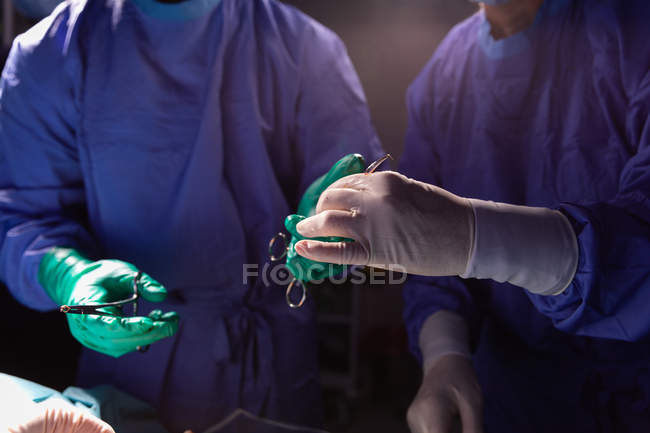 Sezione centrale del chirurgo che tiene le pinze mentre un'altra tiene le forbici durante l'intervento in sala operatoria in ospedale — Foto stock