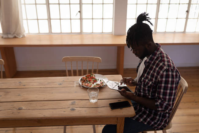 Vue latérale du bel homme afro-américain utilisant une tablette numérique assis sur une chaise à la maison — Photo de stock