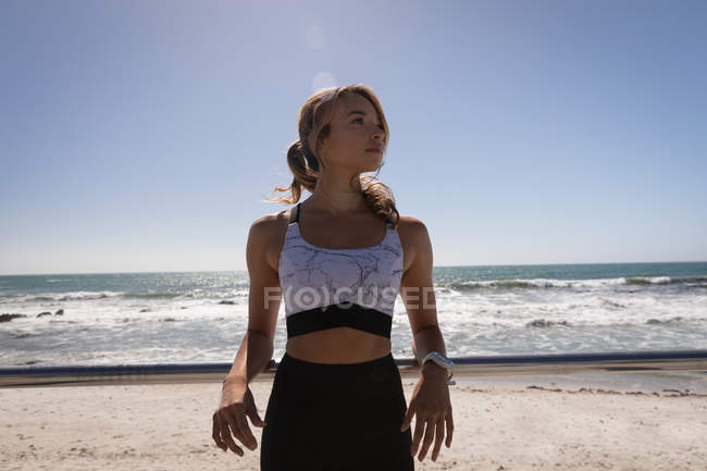 Vue de face femme blonde debout près du bord de mer à la promenade par une journée ensoleillée. Elle regarde ailleurs. — Photo de stock